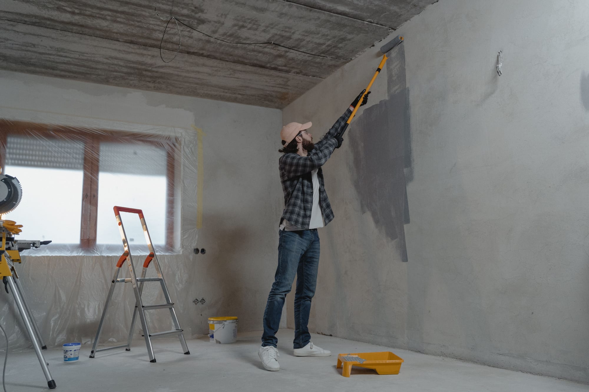 Maler streicht die Wand in einem frisch verputzten Rohbauraum