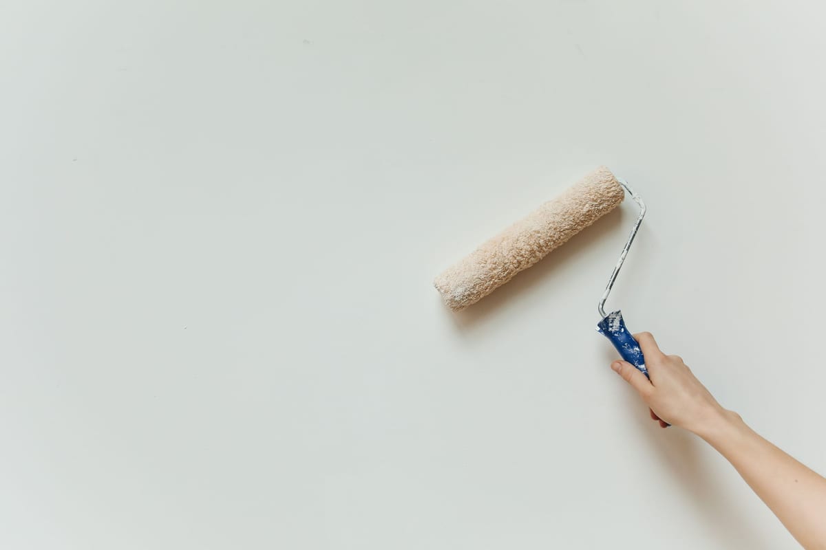 Maler rollt mit der Farbwalze weiße Farbe auf eine glatte Wandfläche