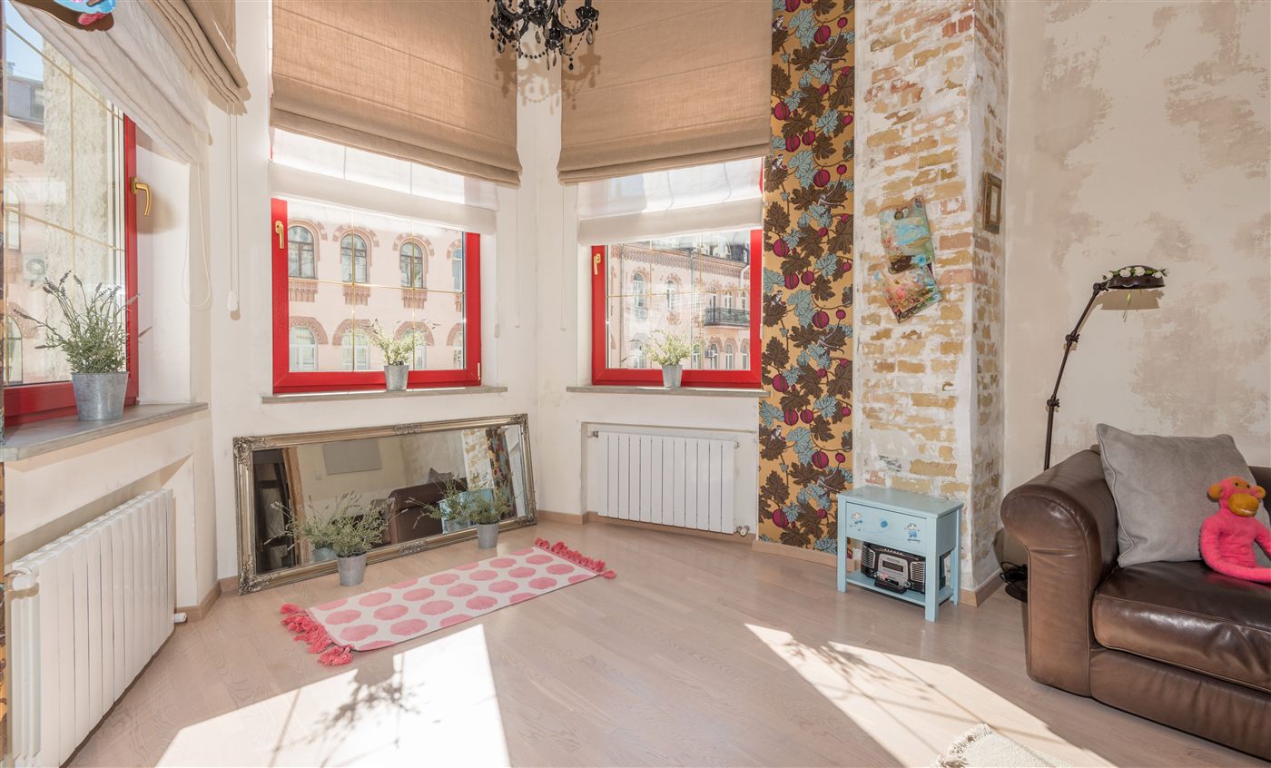 Saniertes Altbau-Wohnzimmer mit Erkerfenstern, freigelegtem Ziegelmauerwerk und Musterwand nach Innenanstrich und Tapezierarbeiten